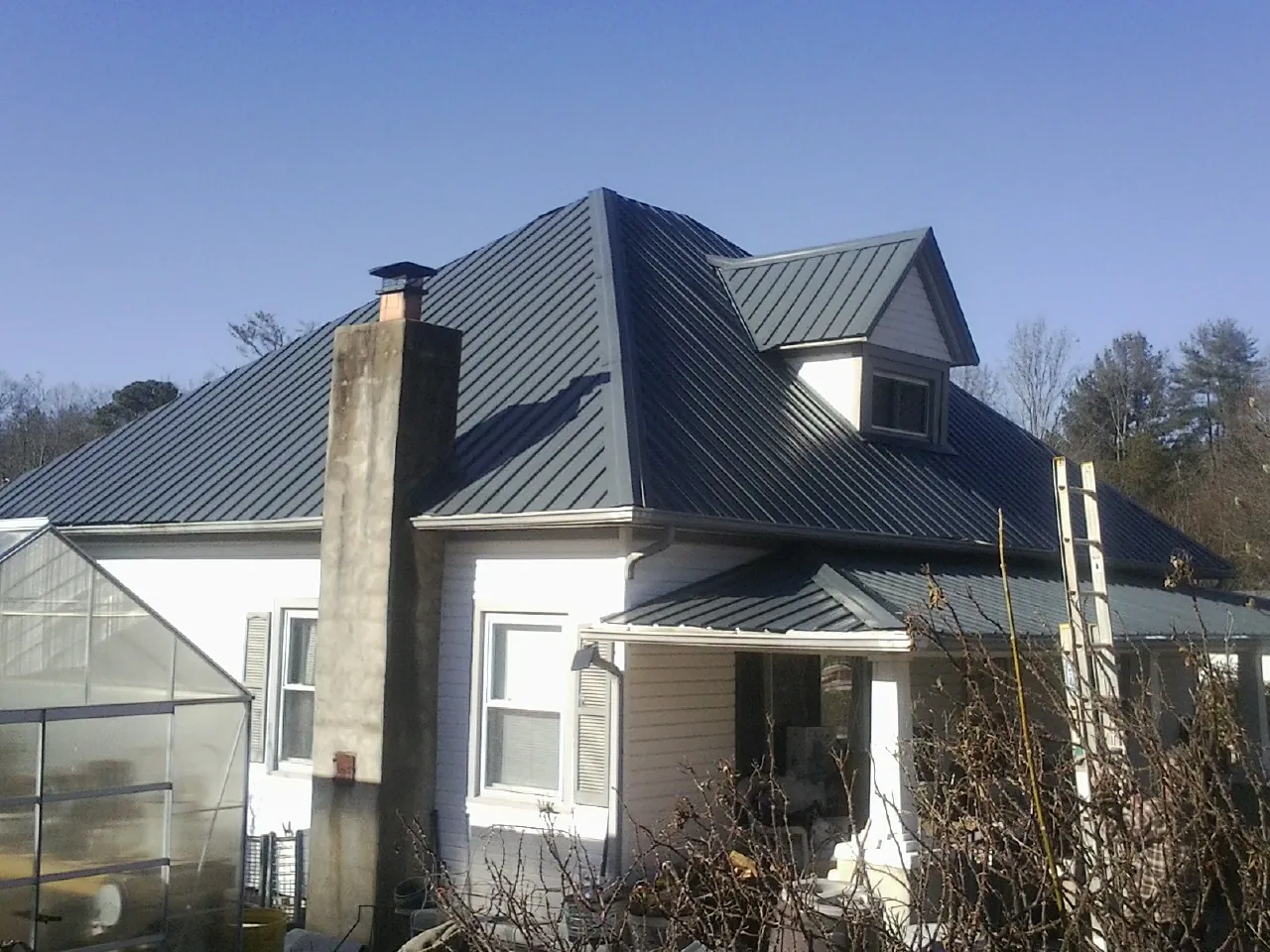 Dark blue standing seam metal roof on a white farmhouse with dormer — Slate & Tile Roof Repair by Roofing Brothers in Royal Center
