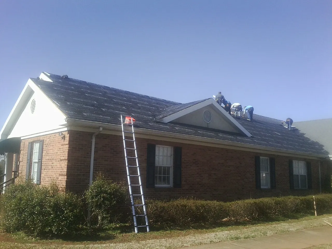 Crew tearing shingles off a brick ranch roof with a ladder set — Metal Roof Repair work by our crew in Royal Center