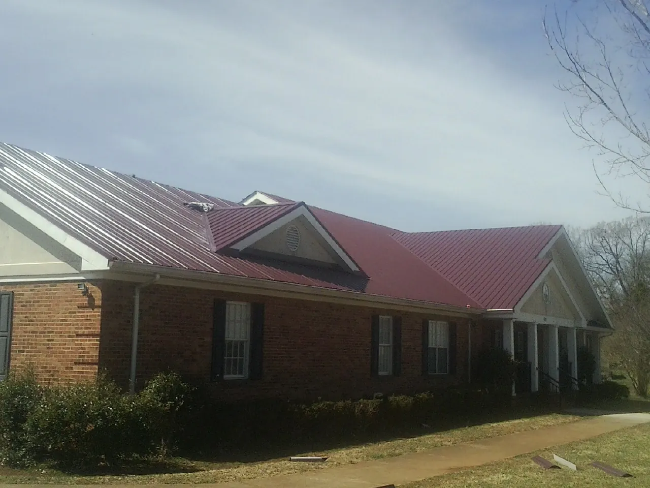 Red metal roof with gabled entries on a long brick building, from a Hail Damage Roof Repair job in Royal Center