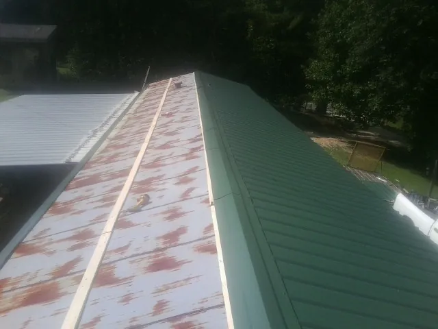 Old rusted panels beside newly installed green metal roofing — Wind Damage Roof Repair by Roofing Brothers in Royal Center