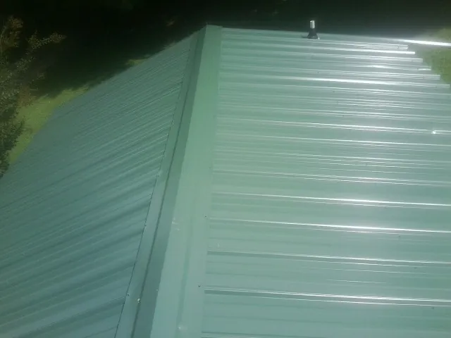New green metal panels meeting at the ridge of a roof — Flat Roof Repair work by our crew in Royal Center