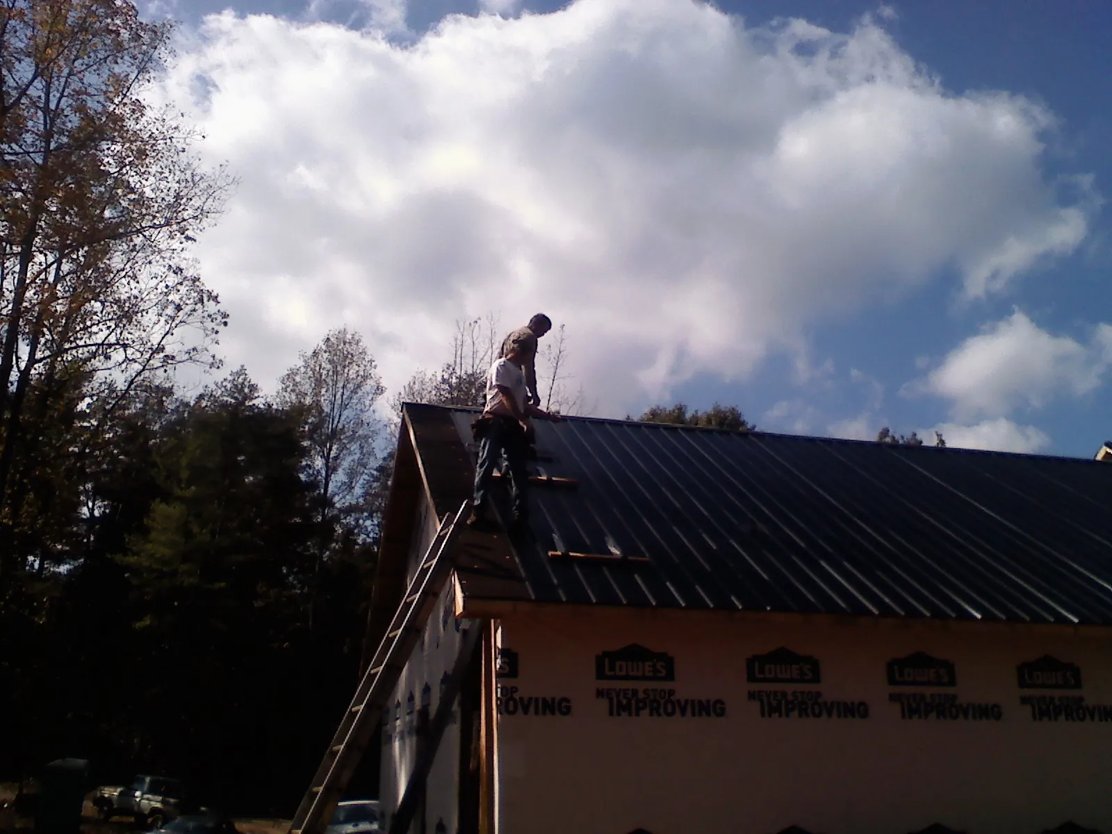 Roofer fastening dark metal panels high against a cloudy sky, from a Roof Inspection job in Royal Center