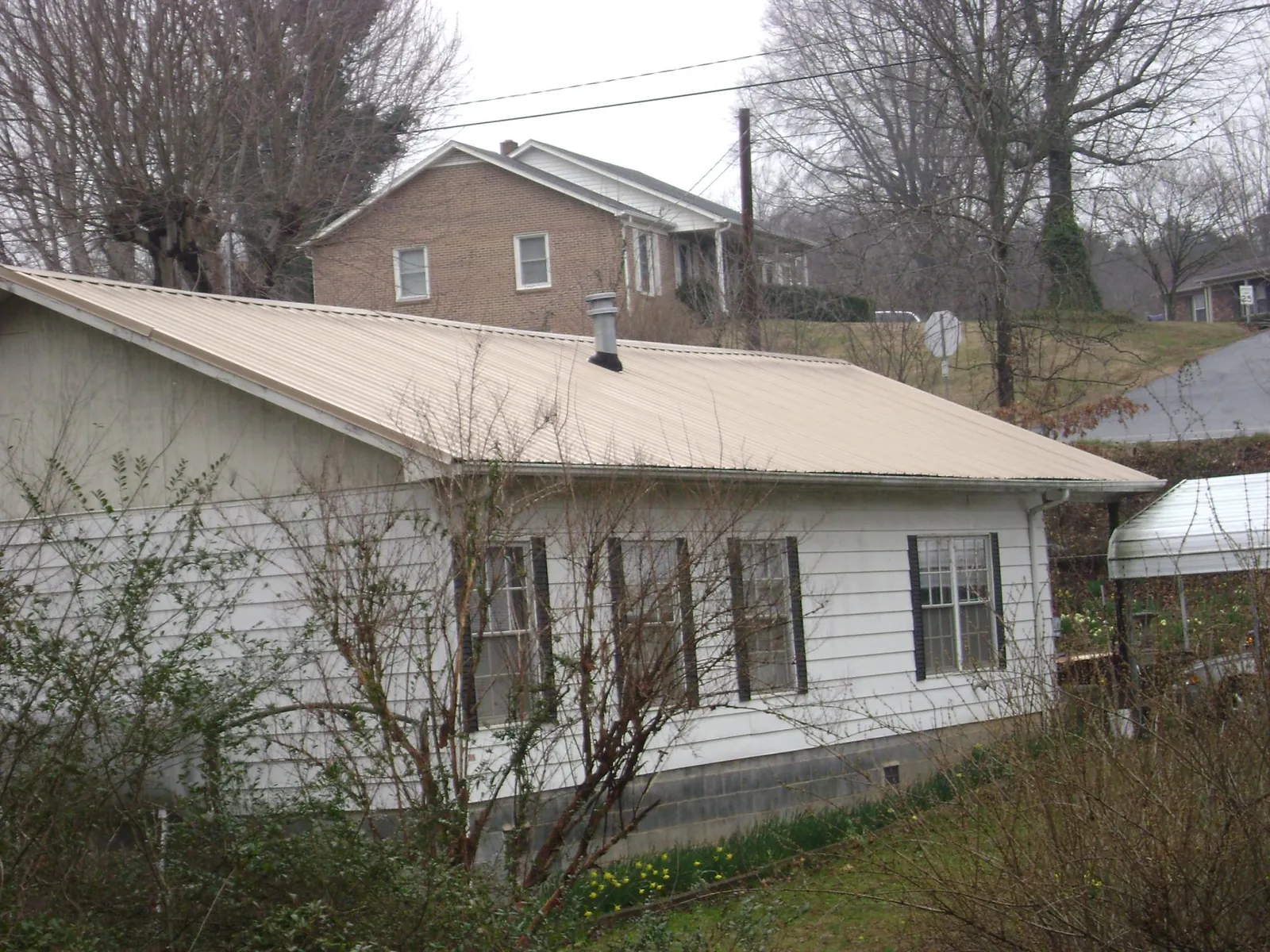 Tan metal roof on a white sided house set into a hillside — Commercial Roofing by Roofing Brothers in Royal Center
