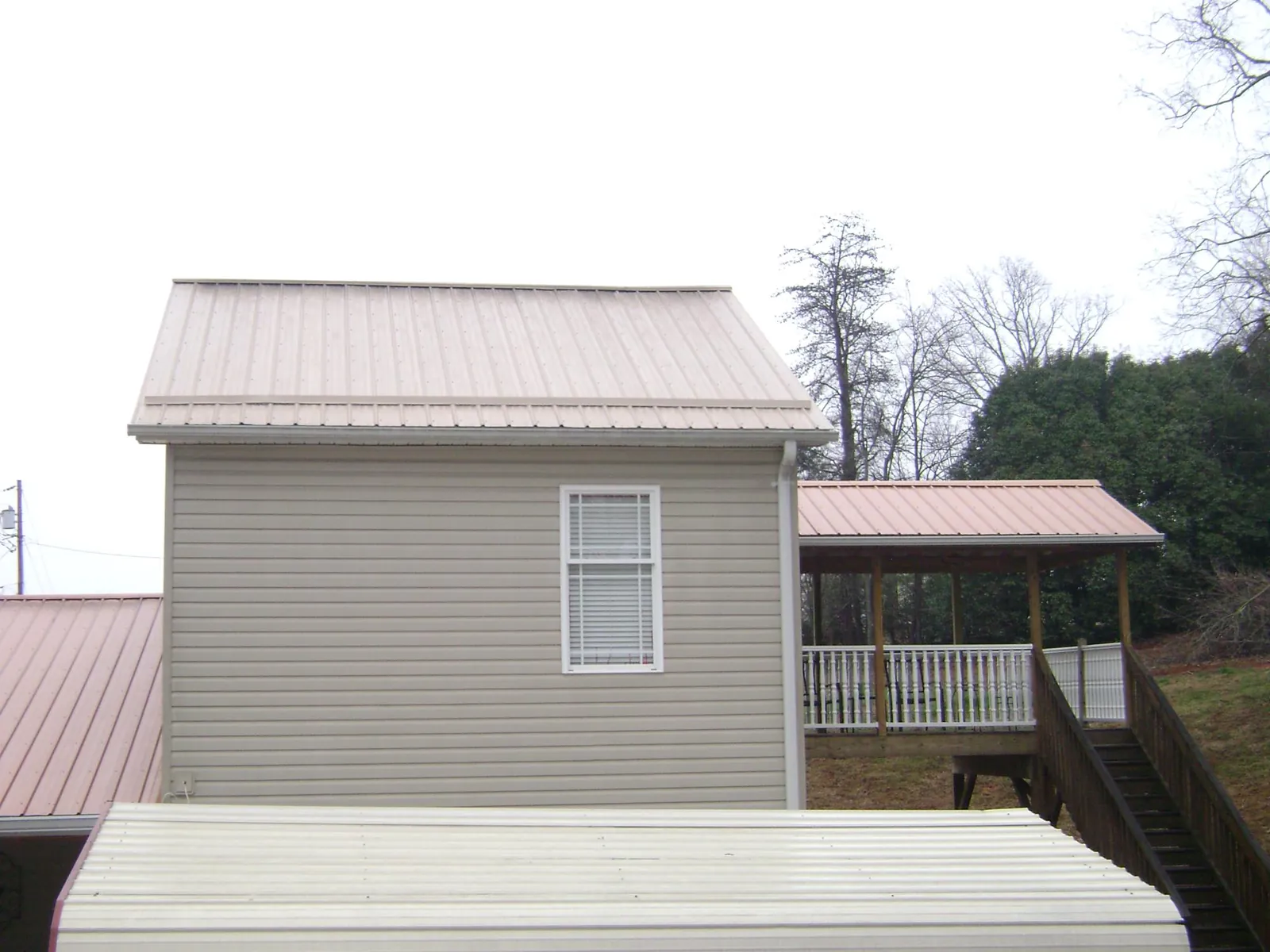 Tan metal roofs on a two story addition and attached porch, from a Roof Replacement job in Royal Center